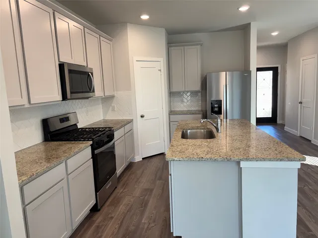 a kitchen with stainless steel appliances granite countertop a sink dishwasher a refrigerator and a stove with wooden floor