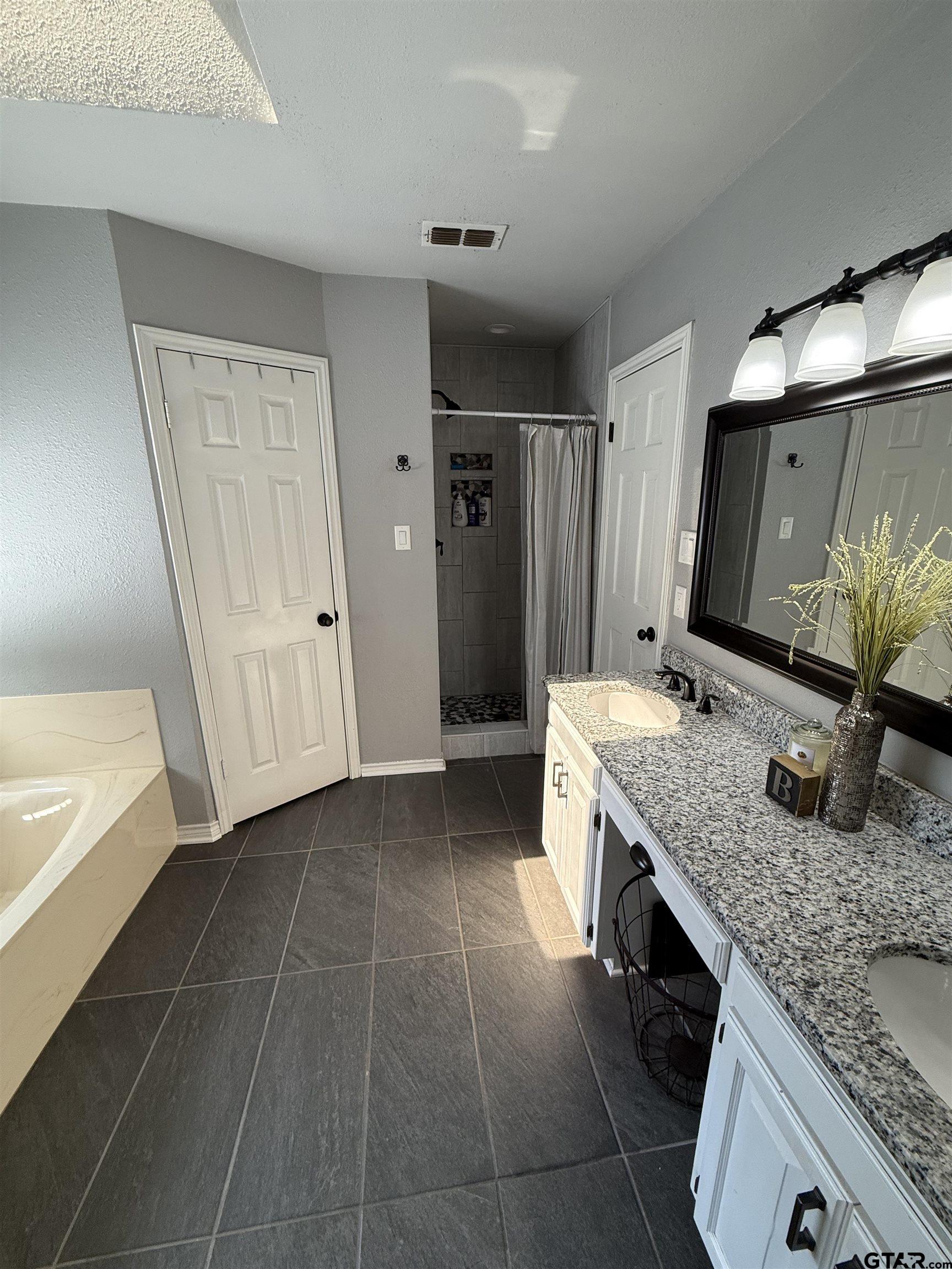 3207 McDonald Road Tyler, TX 75701 - Photo 14 of 24 a bathroom with a granite countertop sink a mirror and a bathtub