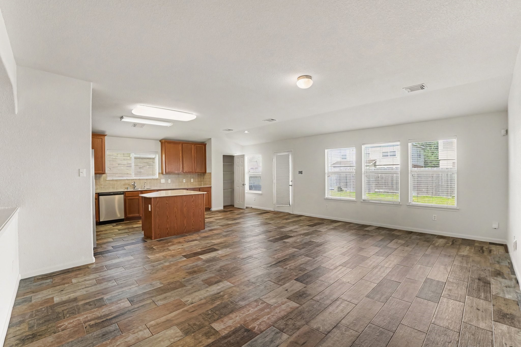 21427 Blooming Rock Lane Spring, TX 77379 - Photo 9 of 32 This photo shows a spacious open-concept living area with wood-look tile flooring. The room features large windows letting in natural light, and an adjacent kitchen with modern appliances, wooden cabinetry, and an island.
