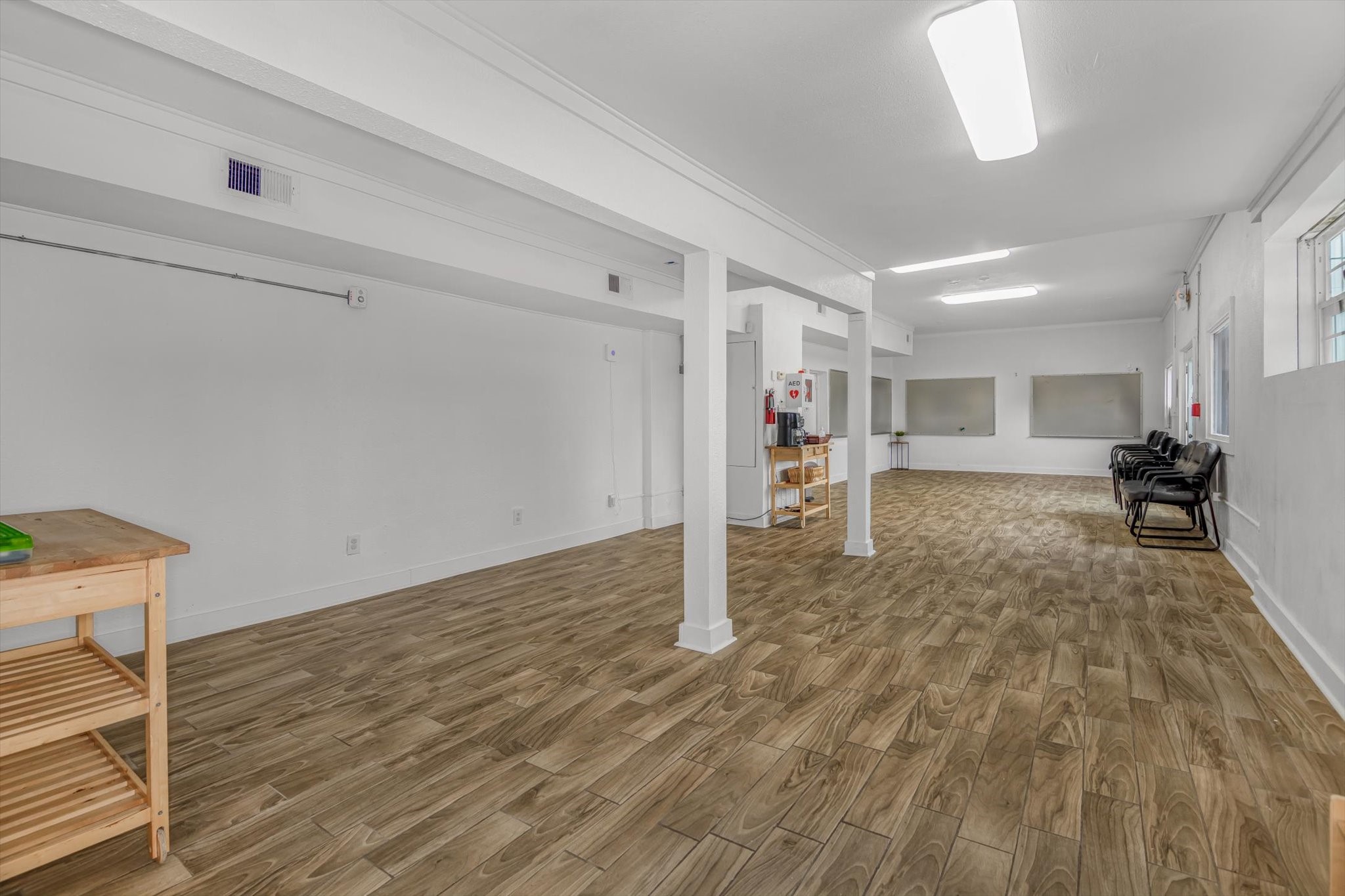 905 43rd Street Galveston, TX 77550 - Photo 7 of 43 Spacious room with wooden flooring, white walls, and ceiling. Features include multiple windows for natural light, ceiling lights, and a few chairs along one wall. Ideal for versatile use or customization.