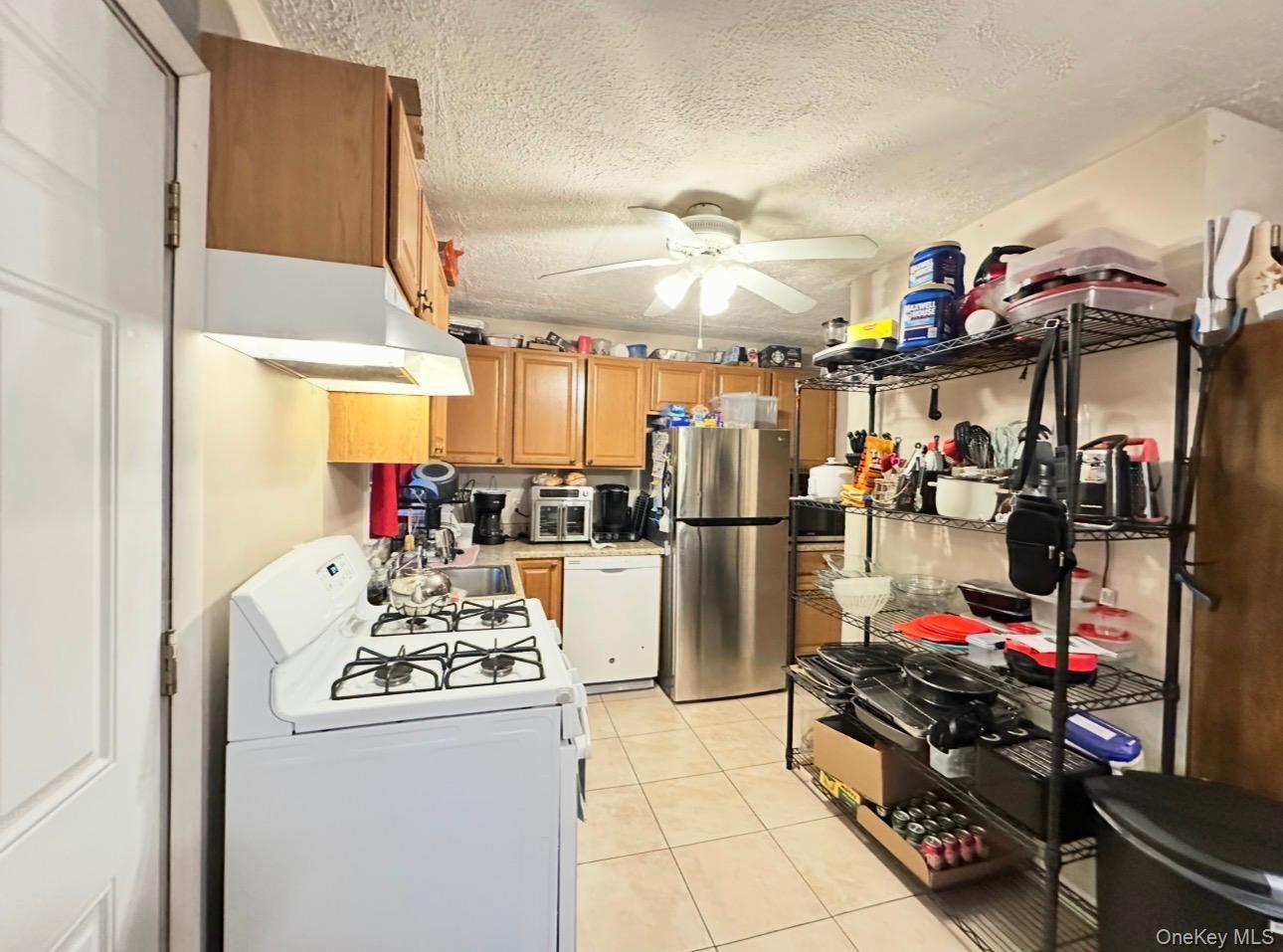 76 Jay Road Centereach, NY 11720 - Photo 3 of 37 First floor. Compact kitchen featuring wood-finish cabinetry, a white gas range with overhead ventilation, a stainless steel refrigerator, and tiled flooring