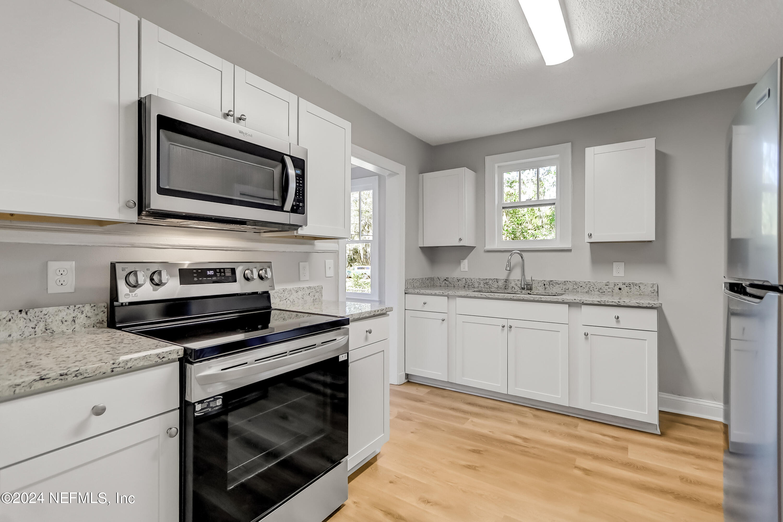 a kitchen with granite countertop white cabinets appliances and a window