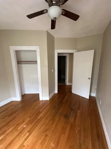 a view of an empty room with wooden floor and a ceiling fan