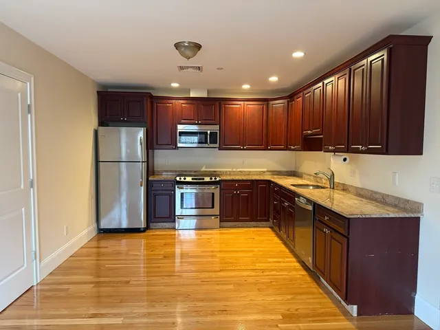 a large kitchen with stainless steel appliances granite countertop a stove top oven a sink dishwasher a refrigerator and a cabinets with wooden floor