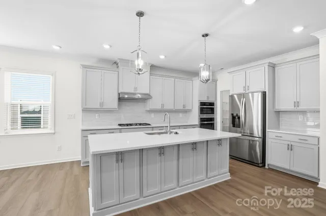 a kitchen with stainless steel appliances granite countertop a refrigerator a sink dishwasher a stove and white cabinets with wooden floor