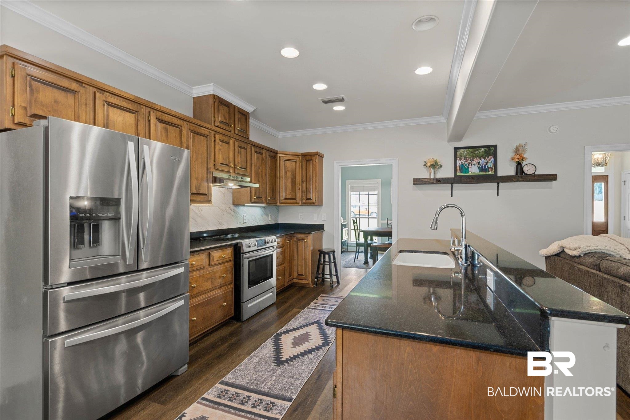 22760 Ridgewood Drive Robertsdale, AL 36567 - Photo 5 of 44 Kitchen with appliances with stainless steel finishes, dark wood-style flooring, brown cabinets, ornamental molding, and tasteful backsplash