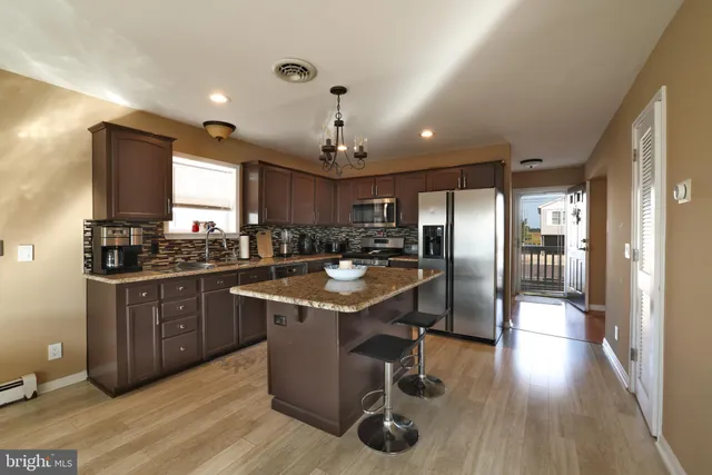 a kitchen with stainless steel appliances granite countertop a refrigerator a sink dishwasher a stove and a dining table with wooden floor