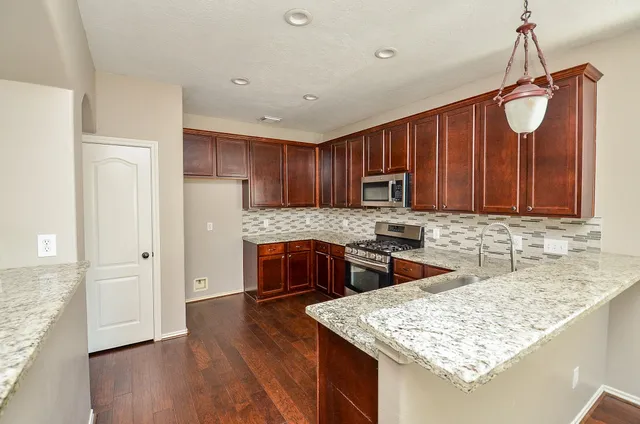 a kitchen with stainless steel appliances granite countertop wooden cabinets a sink and dishwasher a stove top oven with wooden floor