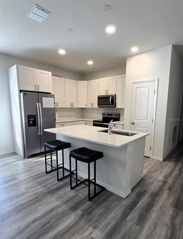 a kitchen with stainless steel appliances a microwave a sink a stove a refrigerator cabinets and wooden floor