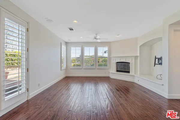 an empty room with wooden floor fireplace and windows