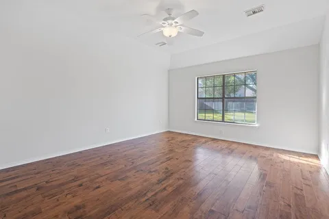 an empty room with wooden floor chandelier fan and windows