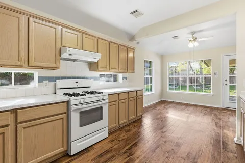 a kitchen with stainless steel appliances granite countertop a stove a sink and white cabinets with wooden floors