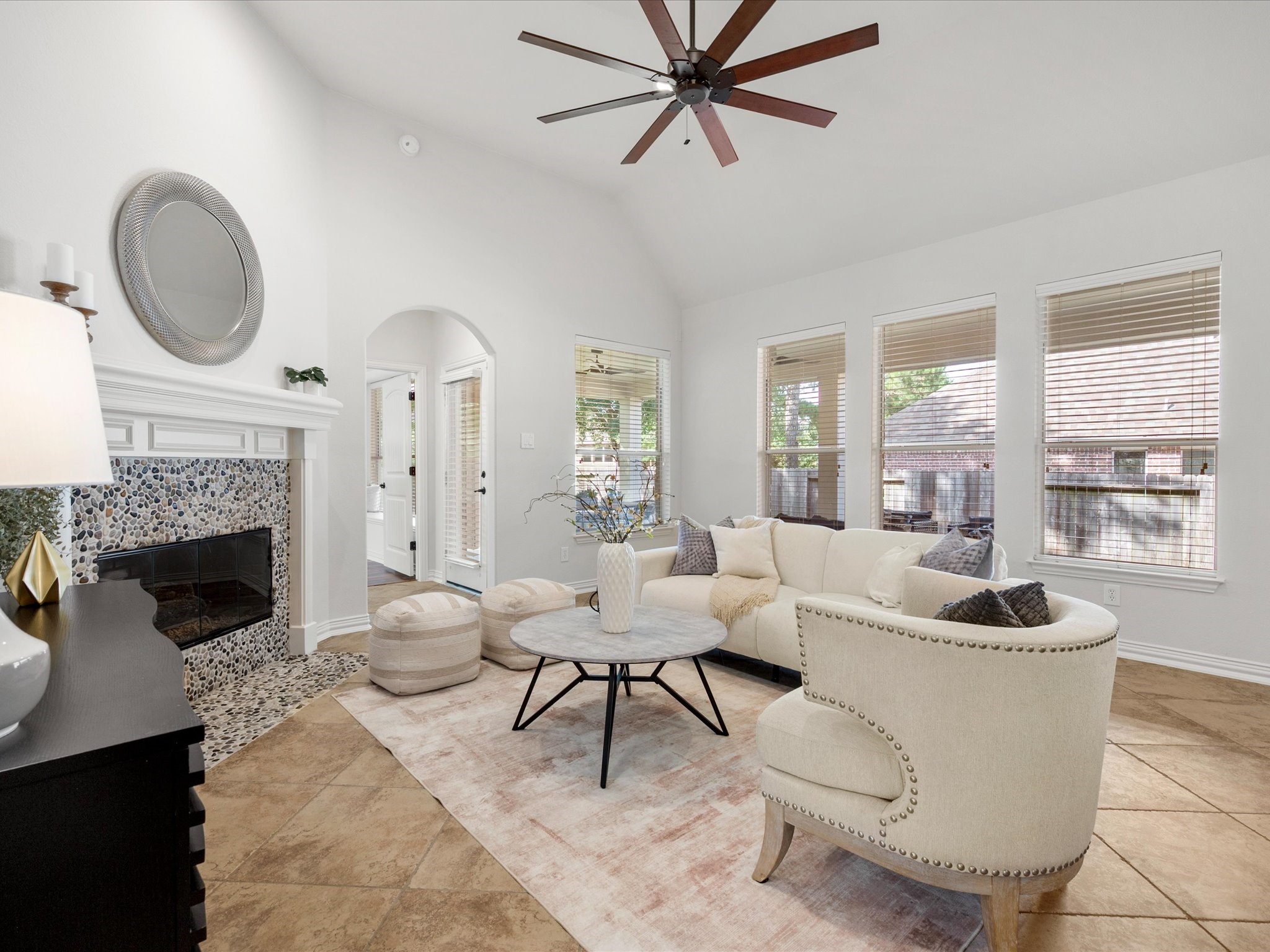323 Arbor Ridge Lane Conroe, TX 77384 - Photo 16 of 40 Here's where everyone lands. Soaring vaulted ceiling, a pebble-tile fireplace that pulls the whole room together, and windows lined up to catch the light all day. Primary suite is just steps away through that arched entry. Room to gather, room to unwind