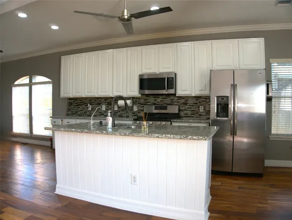 a kitchen with stainless steel appliances granite countertop a refrigerator a stove a sink a microwave a refrigerator and white cabinets with wooden floor