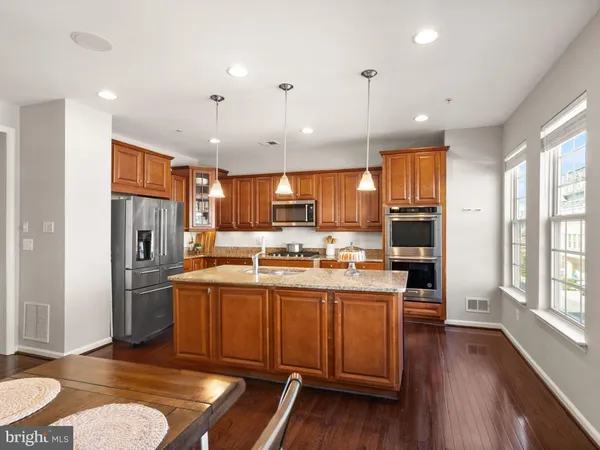 a kitchen with stainless steel appliances granite countertop a refrigerator a sink dishwasher a stove and a dining table with wooden floor