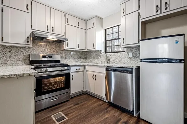 a kitchen with stainless steel appliances granite countertop a refrigerator a stove a sink and white cabinets