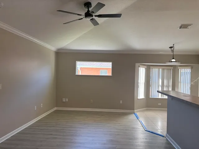 an empty room with wooden floor a ceiling fan and windows