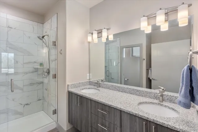 a bathroom with a granite countertop double vanity sink mirror and shower