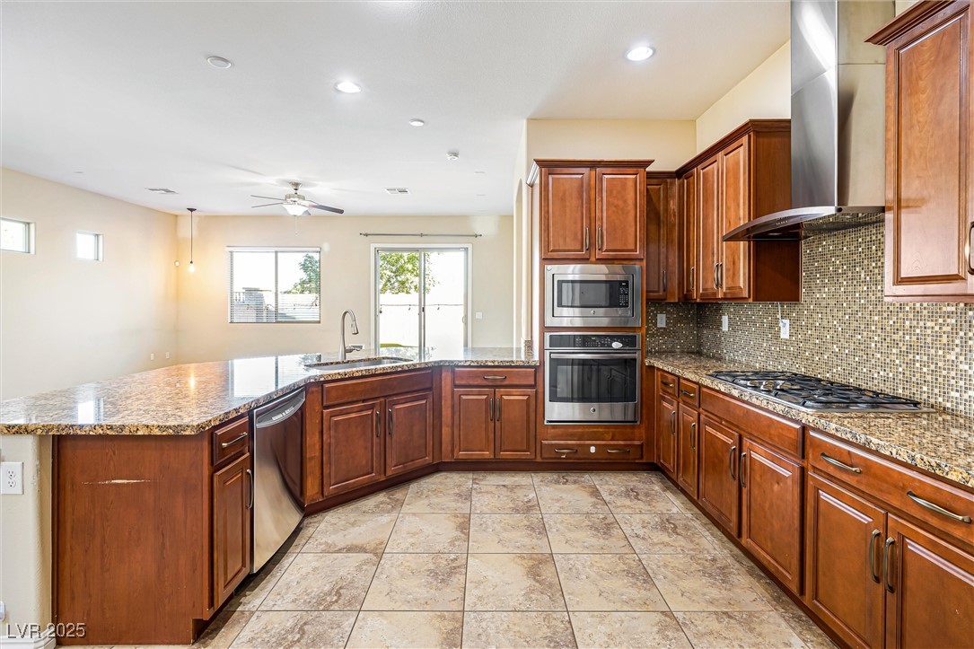 60 Newton Ridge Way Las Vegas, NV 89183 - Photo 11 of 44 Kitchen featuring appliances with stainless steel finishes, wall chimney range hood, light stone counters, decorative backsplash, and recessed lighting
