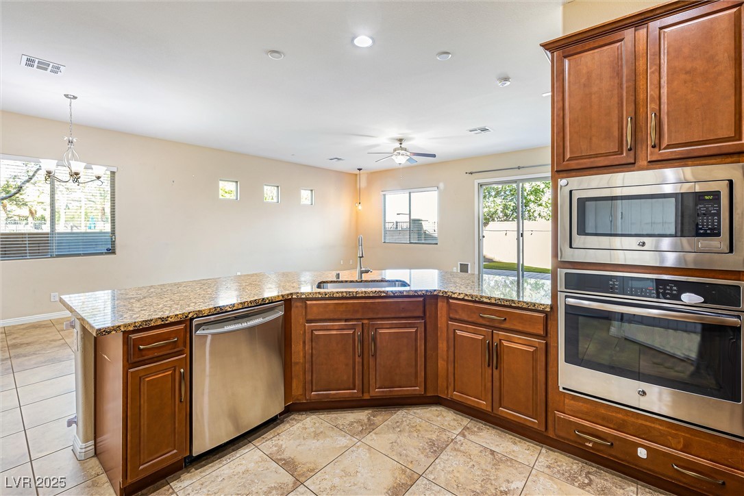 60 Newton Ridge Way Las Vegas, NV 89183 - Photo 12 of 44 Kitchen with stainless steel appliances, light stone countertops, light tile patterned flooring, decorative light fixtures, and brown cabinets