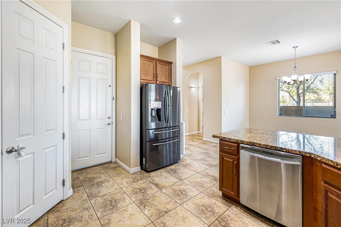 60 Newton Ridge Way Las Vegas, NV 89183 - Photo 13 of 44 Kitchen featuring appliances with stainless steel finishes, dark stone countertops, arched walkways, brown cabinets, and decorative light fixtures