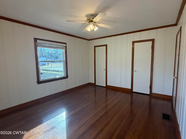 an empty room with wooden floor chandelier fan and windows
