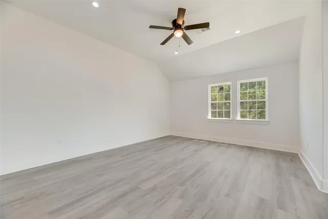 an empty room with wooden floor ceiling fan and windows
