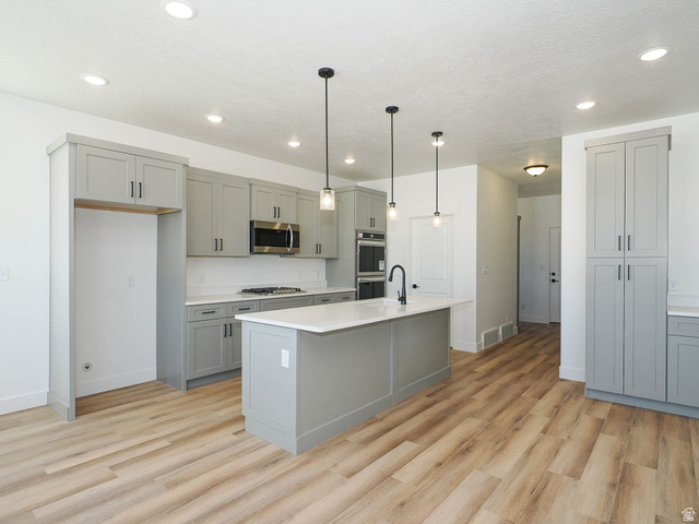 3938 North Wood Road Eagle Mountain, UT 84005 - Photo 14 of 55 Kitchen with gray cabinetry, light wood finished floors, pendant lighting, stainless steel appliances, and light stone countertops