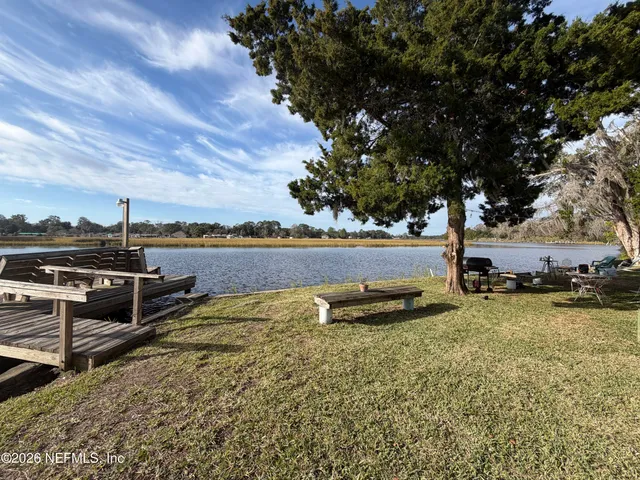 a view of a lake with lawn chairs and large trees