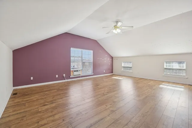 a view of an empty room with wooden floor and a ceiling fan