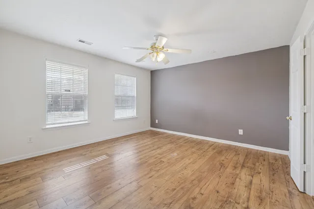 an empty room with wooden floor ceiling fan and windows