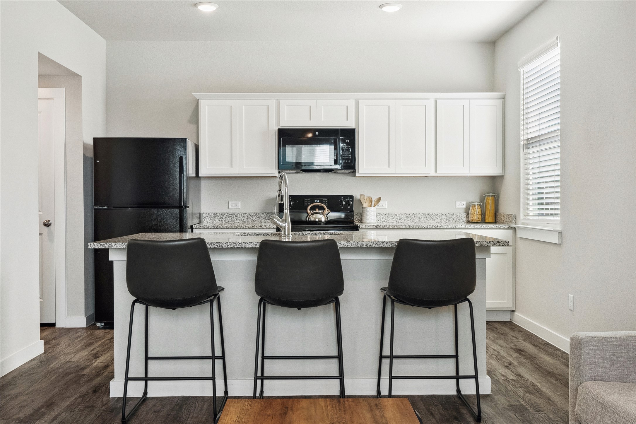 705 Apache Trail, Unit 511 Leander, TX 78641 - Photo 4 of 12 Kitchen with black appliances, white cabinets, a center island with sink, a kitchen breakfast bar, and dark wood-style flooring