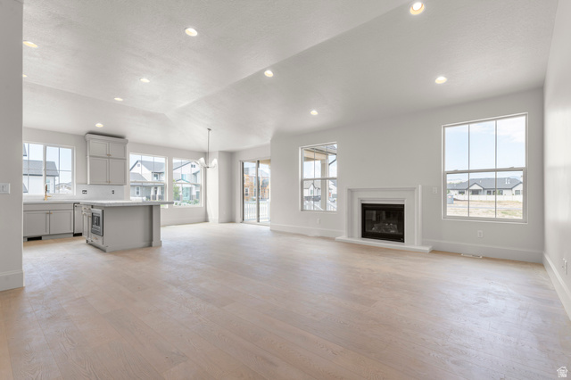 11718 South Halls Crk Road Draper, UT 84020 - Photo 14 of 28 Unfurnished living room featuring recessed lighting, a glass covered fireplace, light wood-style floors, a chandelier, and lofted ceiling