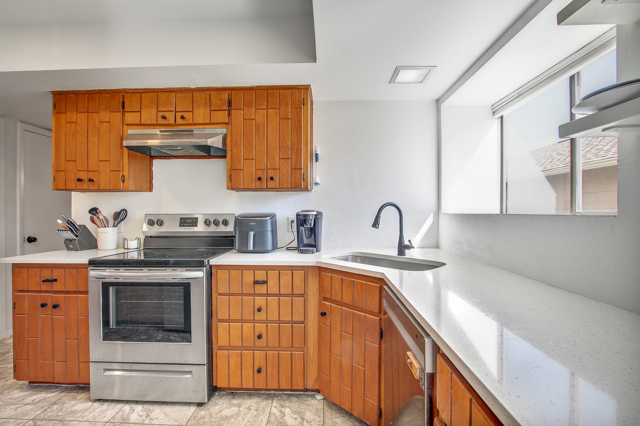 8925 North Plaza, Unit 69 Austin, TX 78753 - Photo 9 of 29 Kitchen featuring appliances with stainless steel finishes, under cabinet range hood, brown cabinetry, and light stone countertops