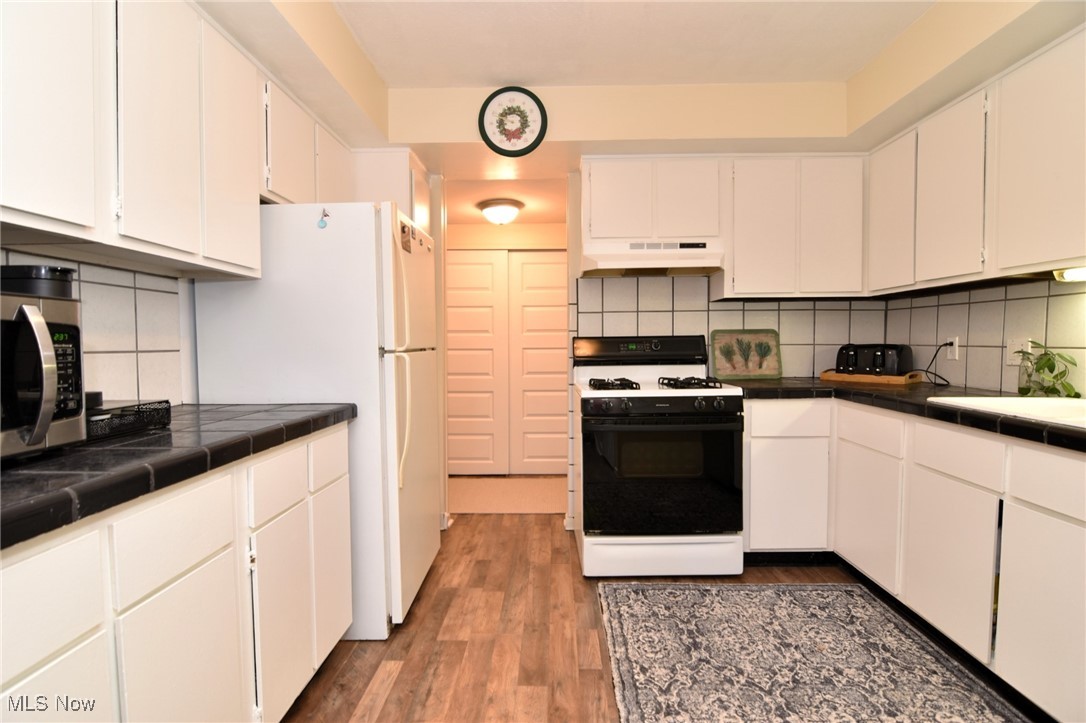 1105 Canyon View Road, Unit 602 Northfield, OH 44067 - Photo 5 of 31 Kitchen featuring tasteful backsplash, white appliances, tile countertops, hardwood / wood-style floors, and white cabinetry