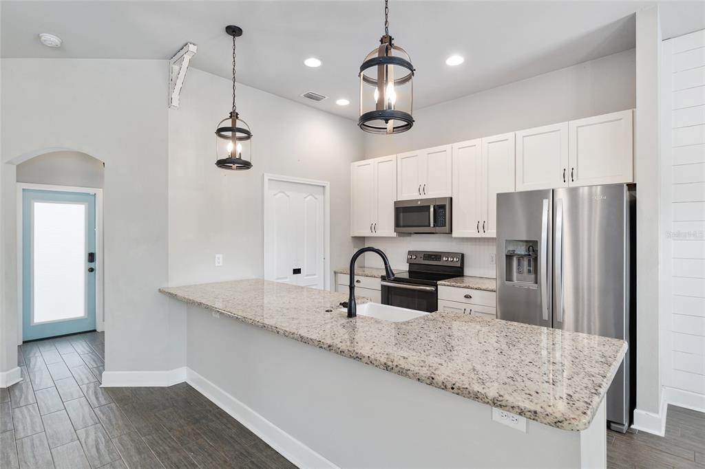 2556 Southwest 118th Terrace Gainesville, FL 32608 - Photo 17 of 72 a kitchen with stainless steel appliances granite countertop a refrigerator a sink dishwasher a oven with white cabinets and wooden floor