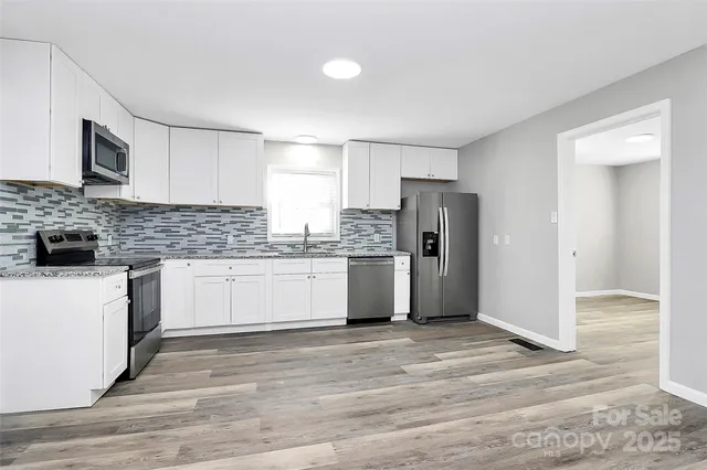 a kitchen with granite countertop a refrigerator oven a sink dishwasher and white cabinets with wooden floor