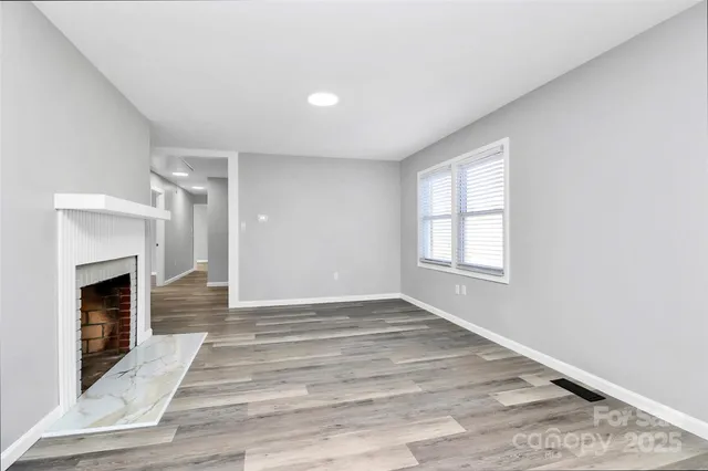 a view of an empty room with wooden floor fireplace and a window