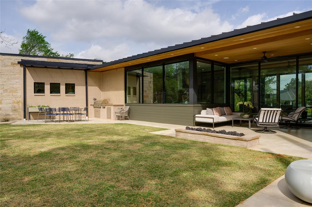 5736 Stonegate Road Dallas, TX 75209 - Photo 27 of 29 Expansive backyard featuring a manicured lawn, outdoor kitchen with built-in grill, stone fire pit, and a covered patio with a wood-paneled ceiling
