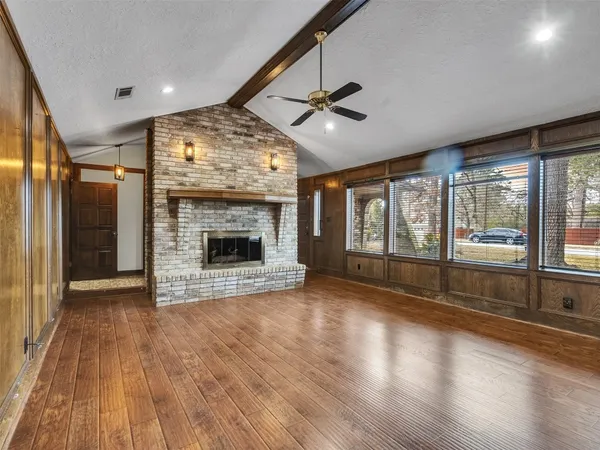 an empty room with wooden floor fireplace cabinet and windows