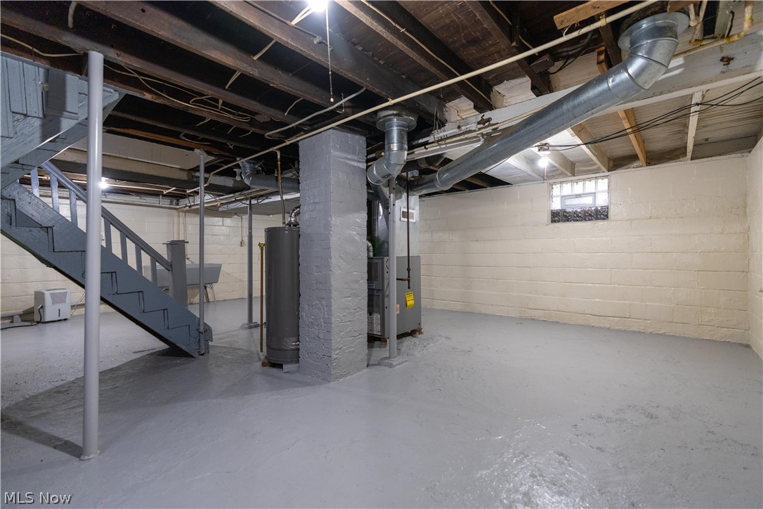 796 Dayton Street Akron, OH 44310 - Photo 20 of 25 Spacious basement area featuring a painted concrete floor, exposed ceiling joists, utility sink, block foundation walls, and a staircase with painted wood railings