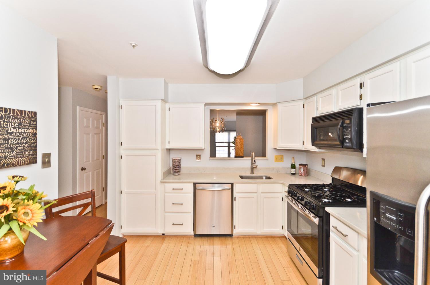 9923 Raintree Way Clinton, MD 20735 - Photo 6 of 30 a kitchen with a sink dishwasher a stove a microwave oven and a dining table with wooden floor