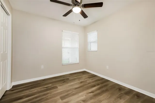 an empty room with wooden floor ceiling fan and windows