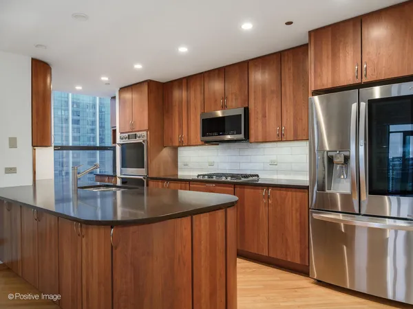 a kitchen with kitchen island granite countertop wooden cabinets a refrigerator a stove and a sink with wooden floor