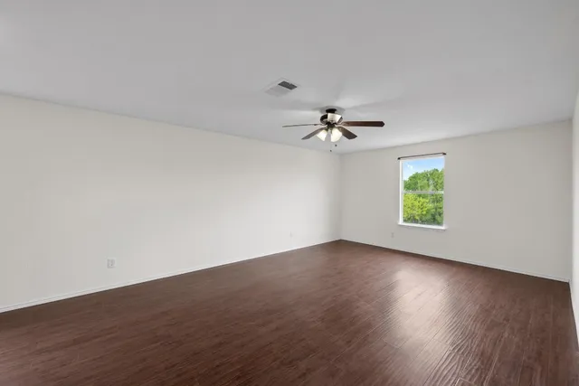 an empty room with wooden floor chandelier fan and windows