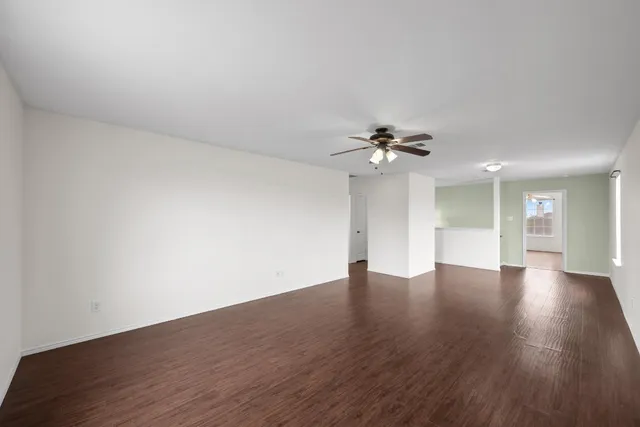 a view of an empty room with wooden floor and a ceiling fan