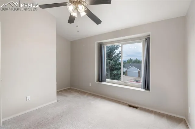 an empty room with chandelier fan and windows