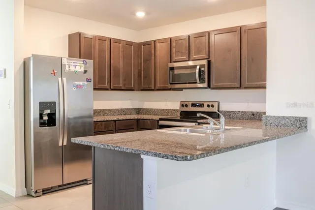 a kitchen with stainless steel appliances granite countertop a refrigerator a stove and a sink with wooden floor