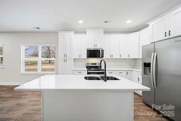 a kitchen with a refrigerator a stove a sink and white cabinets with wooden floor