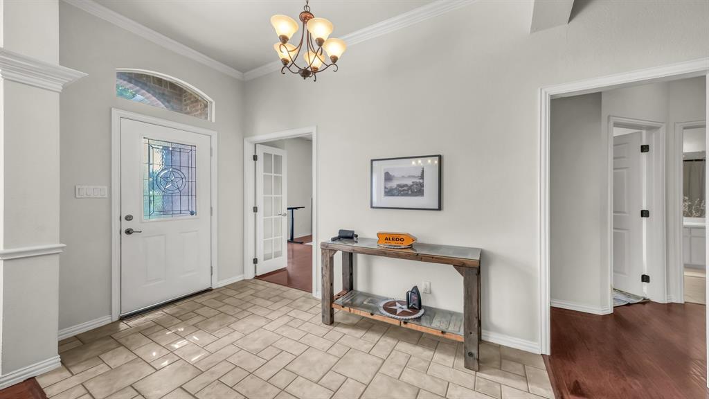 203 Mockingbird Lane Aledo, TX 76008 - Photo 9 of 37 Entryway featuring tile flooring, a decorative glass front door with an arched transom window, crown molding, and a chandelier